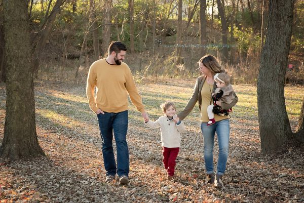 family walking through fall leaves holding hands