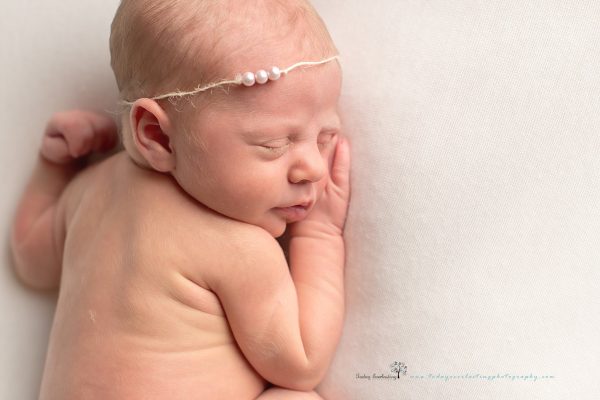 Baby girl sleeping with delicate pearl headband on soft white background