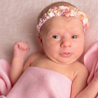 Cute baby girl wearing pink flowered headband with pink wrap on soft pink background