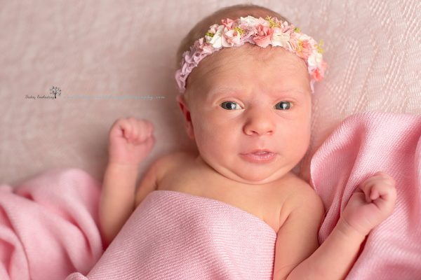 Cute baby girl wearing pink flowered headband with pink wrap on soft pink background