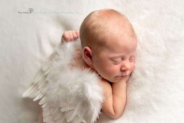 Sweet baby girl wearing angel wings sleeping on soft white background