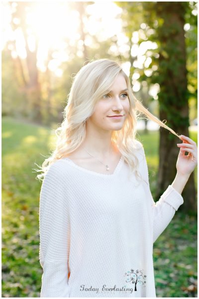 beautiful blonde graduate wearing white lacy dress in etherial woods with golden haze