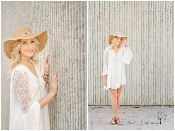 Gorgeous blonde high school graduate in white lacy dress with floppy hat against textured stone background