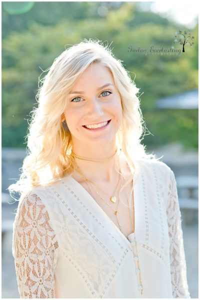 Beautiful blonde graduate with bright smile and lacy white dress in golden light against soft green background