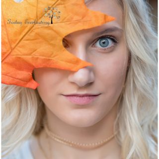 Bold artistic image with vivid colored leaf in the foreground partially covering young ladie's bright blue eyes.