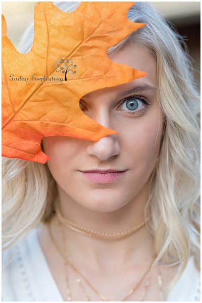 Bold artistic image with vivid colored leaf in the foreground partially covering young ladie's bright blue eyes.