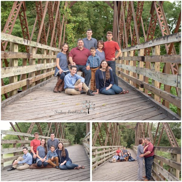 Large family posed on old wooden bridge, children seated together, children in background and parents in romantic pose in foreground.