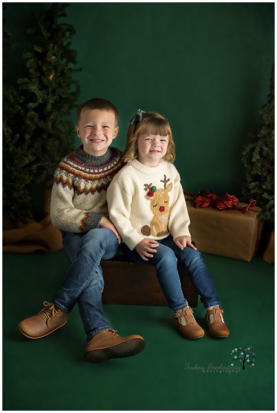 Cute brother and sister wearing Christmas sweaters with evergreen background