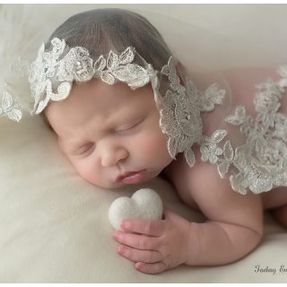 newborn girl holding a white heart draped in her mother's wedding veil