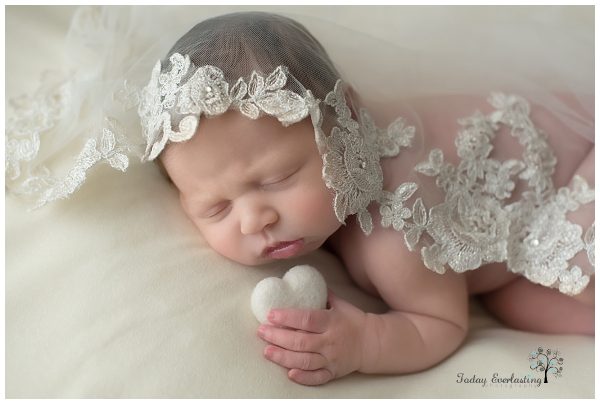 newborn girl holding a white heart draped in her mother's wedding veil