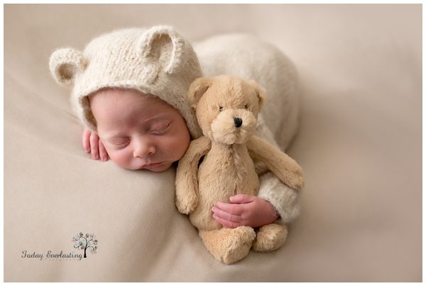 Newborn baby boy dressed in a bear outfit snuggling a teddy bear.
