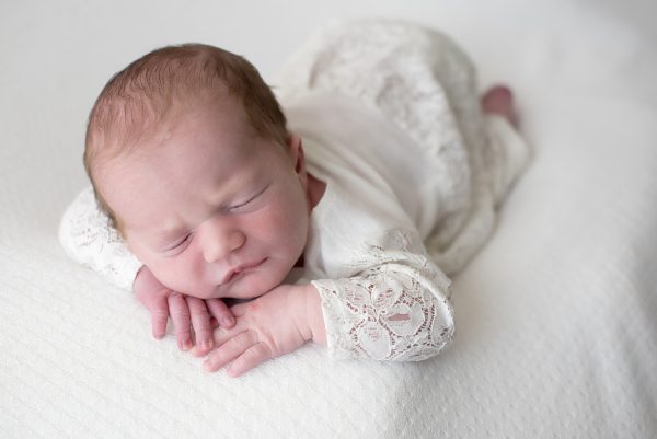 newborn girl dressed in white with her chin resting on her hands