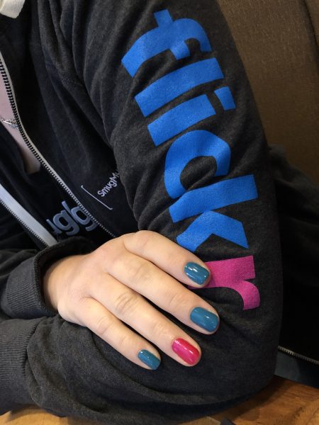 A hand is resting on the arm of a jacket with flickr written on it. The fingernails are painted to match the flickr colors.