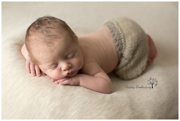 Sleeping newborn baby posed safely on a cream blanket