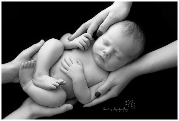 A black & white photo of a sleeping newborn with both parents hands.