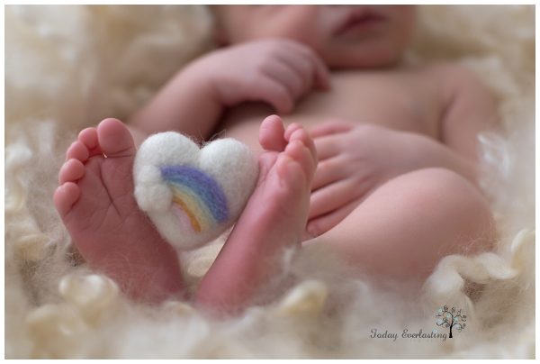 Felted heart with a rainbow on it held between a newborn's feet