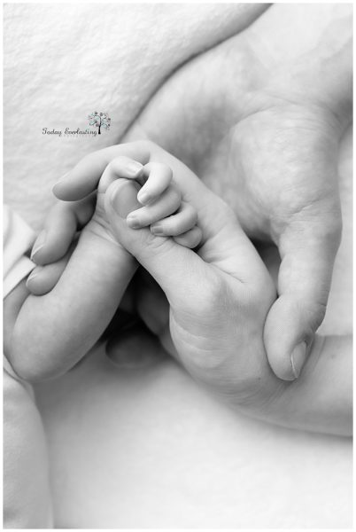 black & white photo showing a newborn's fingers wrapped around its mother's thumb