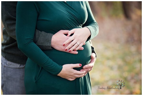 Maternity portrait of a couple with their hands joined together holding the baby bump.