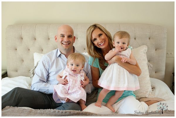 A mother, father, and their two young daughters are sitting on a bed.