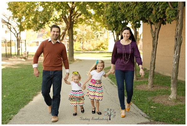 A mother, father, and their two young daughters are walking together and smiling