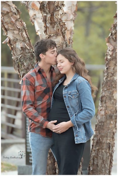 A man is kissing the side of his wife's head. They both have their hands on her baby bump.