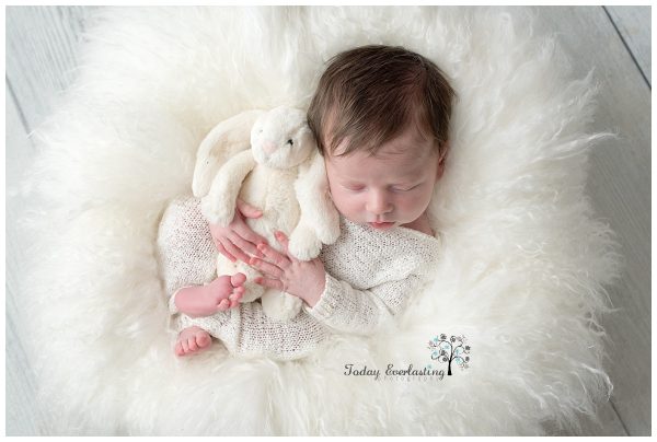A newborn baby boy is nestled in soft white fur, holding a bunny in Morris IL